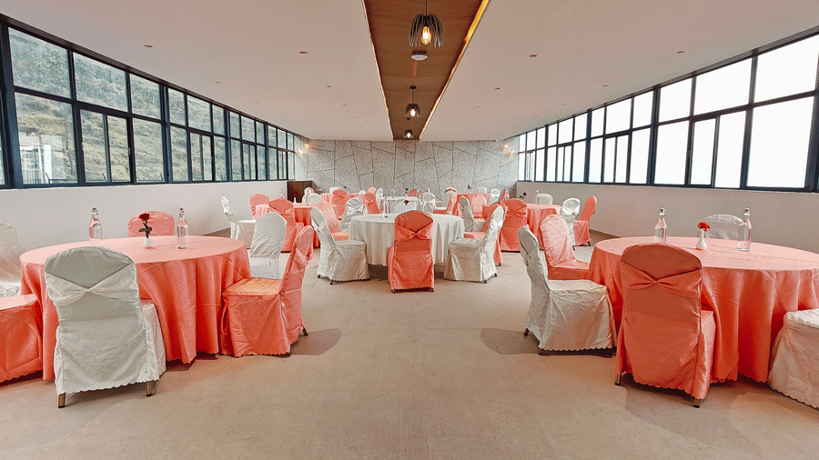 A long banquet hall features 2 rows of round tables with peach and white decor at Bliss Casa Mila By Bergamont Hotels, Kodaikanal.