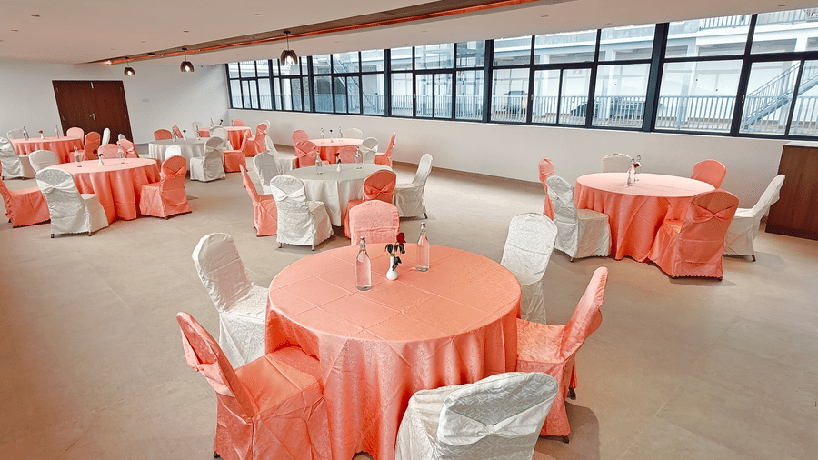 Round tables with peach and white linens are spread across a brightly lit hall at Bliss Casa Mila By Bergamont Hotels, Kodaikanal.