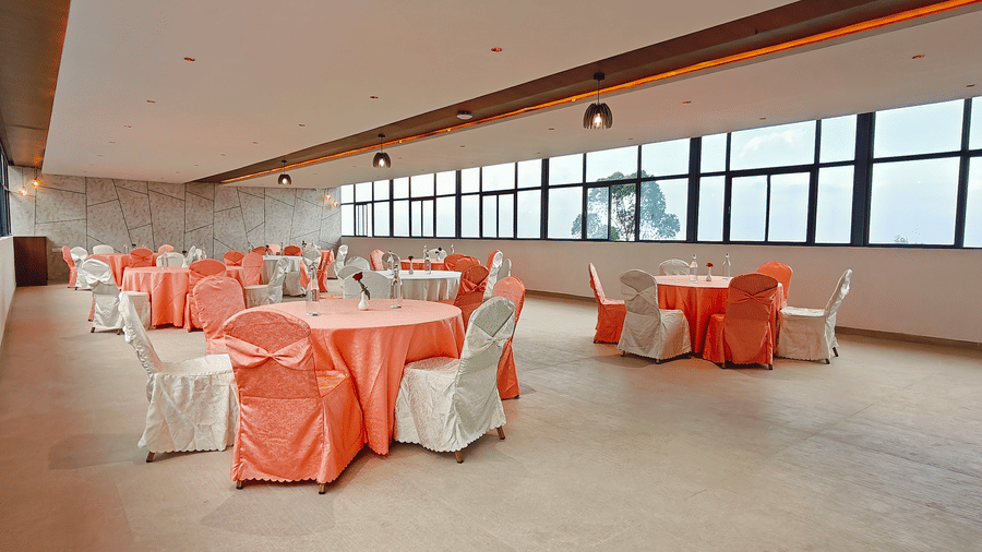 An expansive indoor event space shows several round tables with peach-coloured fabrics at Bliss Casa Mila By Bergamont Hotels, Kodaikanal.