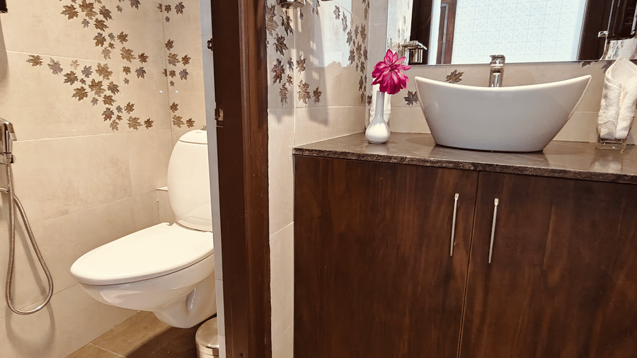 An interior view of a bathroom showing a white toilet, a grey bowl sink, and floral wall tiles at Bliss Casa Mila By Bergamont Hotels, Kodaikanal.