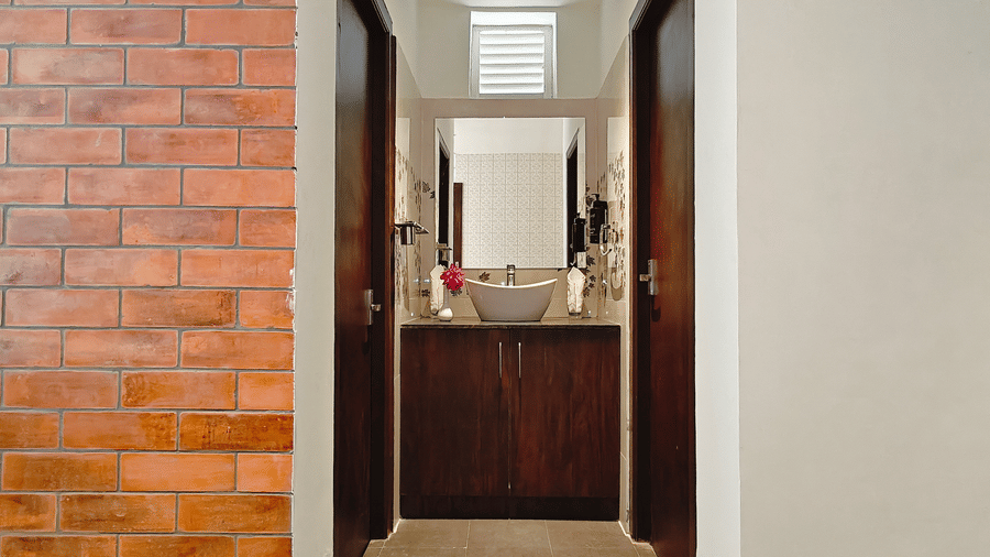 A view of a bathroom vanity with a grey bowl sink and a wooden cupboard between 2 dark doors at Bliss Casa Mila By Bergamont Hotels, Kodaikanal.