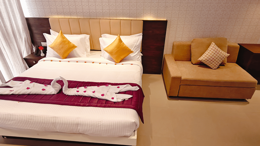 A double bed with swan-shaped towel art positioned next to a brown sofa with 1 cushion at Bliss Casa Mila By Bergamont Hotels, Kodaikanal.