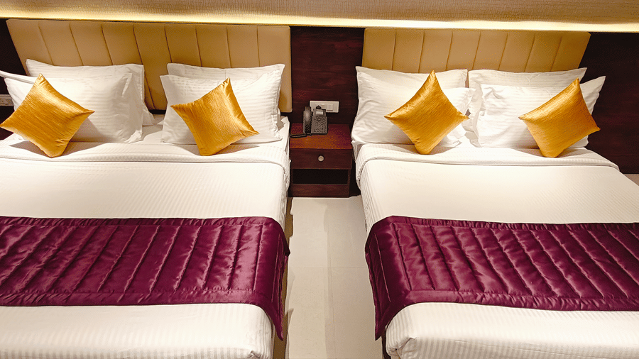 2 beds with white bedding, yellow cushions, and purple runners separated by a dark wood bedside table at Bliss Casa Mila By Bergamont Hotels, Kodaikanal.