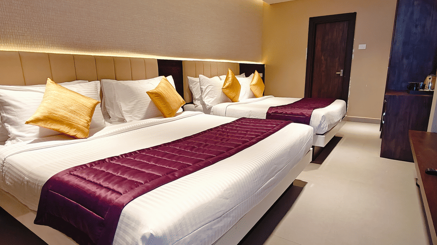 2 beds with white pillows, yellow cushions, and purple runners in a room with a wooden door at Bliss Casa Mila By Bergamont Hotels, Kodaikanal.