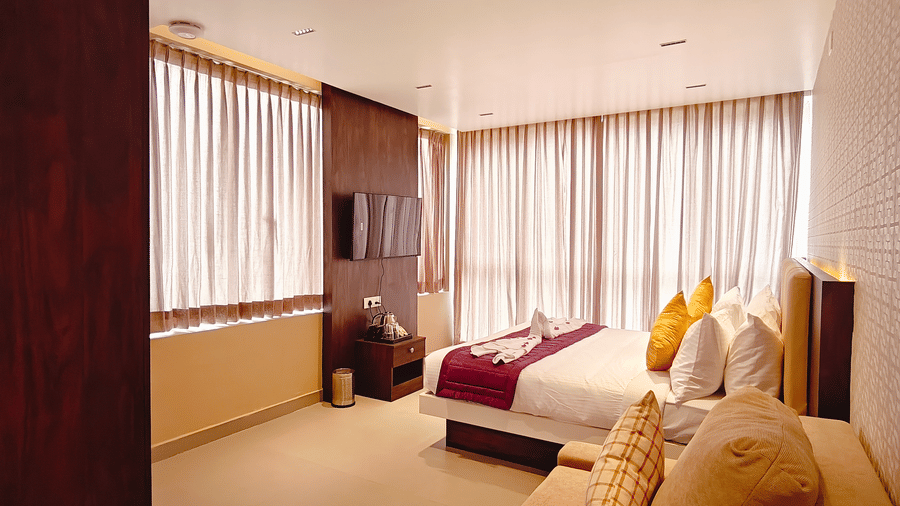 A bedroom view showing a television mounted on a wooden panel next to a bed with 2 yellow cushions at Bliss Casa Mila By Bergamont Hotels, Kodaikanal.