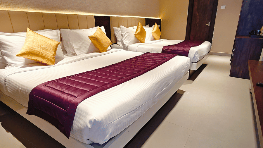 White beds with purple runners are arranged in a brightly lit hotel room at Bliss Casa Mila By Bergamont Hotels, Kodaikanal.