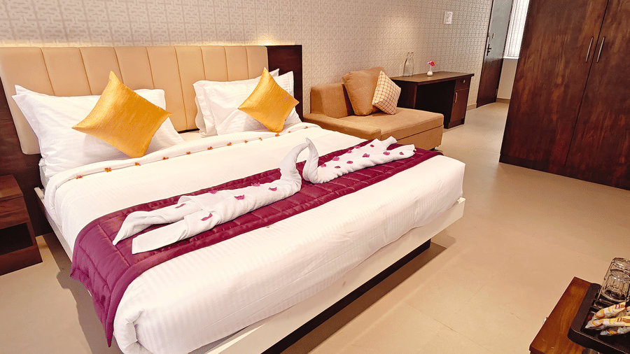 A double bed with white linens, 2 yellow cushions, and 2 towels folded into swan shapes at Bliss Casa Mila By Bergamont Hotels, Kodaikanal.