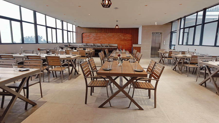 A spacious dining room features multiple wooden tables and a brick accent wall at Bliss Casa Mila By Bergamont Hotels, Kodaikanal.
