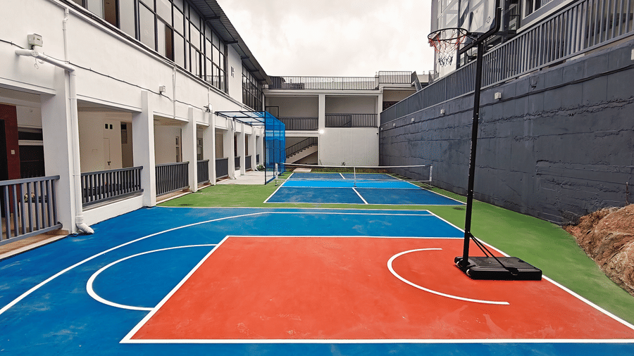 A blue and orange basketball court area situated next to a white building at Bliss Casa Mila By Bergamont Hotels, Kodaikanal.