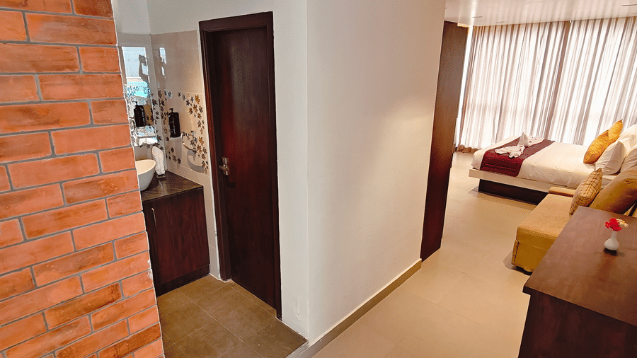 A perspective showing a brick wall, a bathroom entrance, and the main bedroom area with a bed at Bliss Casa Mila By Bergamont Hotels, Kodaikanal.