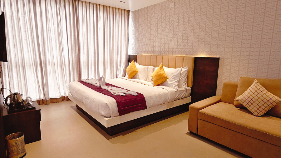 A suite room featuring a double bed with towel art, a sofa, and large windows with curtains at Bliss Casa Mila By Bergamont Hotels, Kodaikanal.