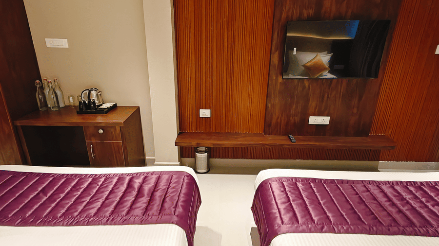 A wall-mounted television is set into a wooden panel opposite the foot of 2 beds at Bliss Casa Mila By Bergamont Hotels, Kodaikanal.