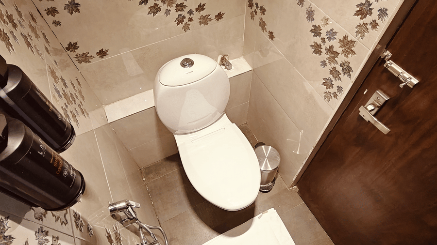 A top-down view of a white toilet next to a dark wooden door and 2 black soap dispensers at Bliss Casa Mila By Bergamont Hotels, Kodaikanal.