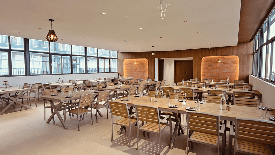 Dining area with wooden furniture and large windows along the side at Bliss Casa Mila By Bergamont Hotels, Kodaikanal.
