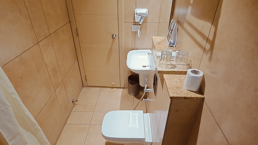 Clean and modern bathroom in the Deluxe Double Room at Cholaa Dynasty, Kumbakonam equipped with a shower area, wash basin, mirror, and essential amenities ensuring a convenient and hygienic stay experience
