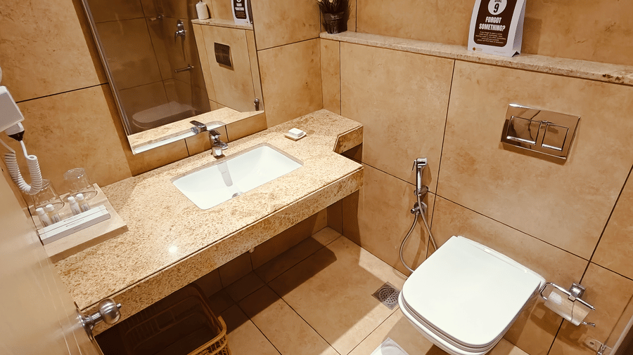 Bathroom vanity with washbasin in the Deluxe Single Room at Chola Dynasty, Kumbakonam featuring a sleek countertop, mirror, and modern fittings providing convenience and comfort.
