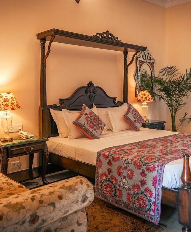 A Deluxe Room with a four-poster bed, a window, a sofa, and elegant decor with warm lighting - Khas Bagh, Jaipur