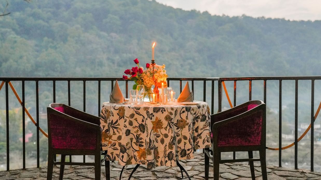 A patio with a table and chairs, decorated with flowers and candles, overlooking a valley with trees and mountains.