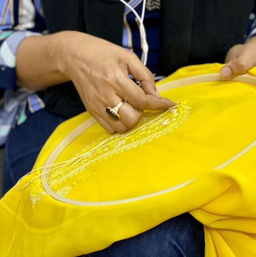 Close up of a woman weaving a peace of yellow-coloured cloth locked in an embroidery ring with thread and needle.