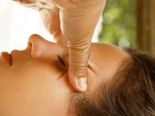 A woman with her eyes closed is receiving a relaxing facial massage on her temple