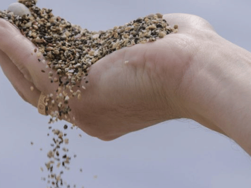 A hand holds a scoop of small pebbles and sand, which are slowly falling through the fingers.