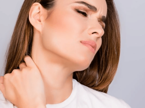 A woman, eyes closed, is massaging the side of her neck and shoulder