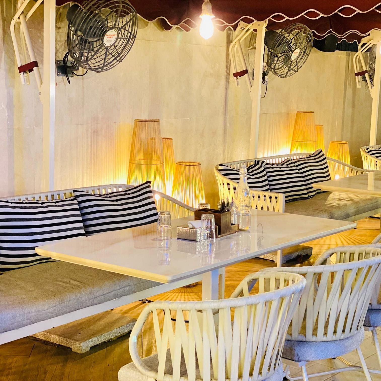 Indoor dining area with white chairs, wooden tables, and striped cushions at Hotel Mumbai House Mindspace, Malad.