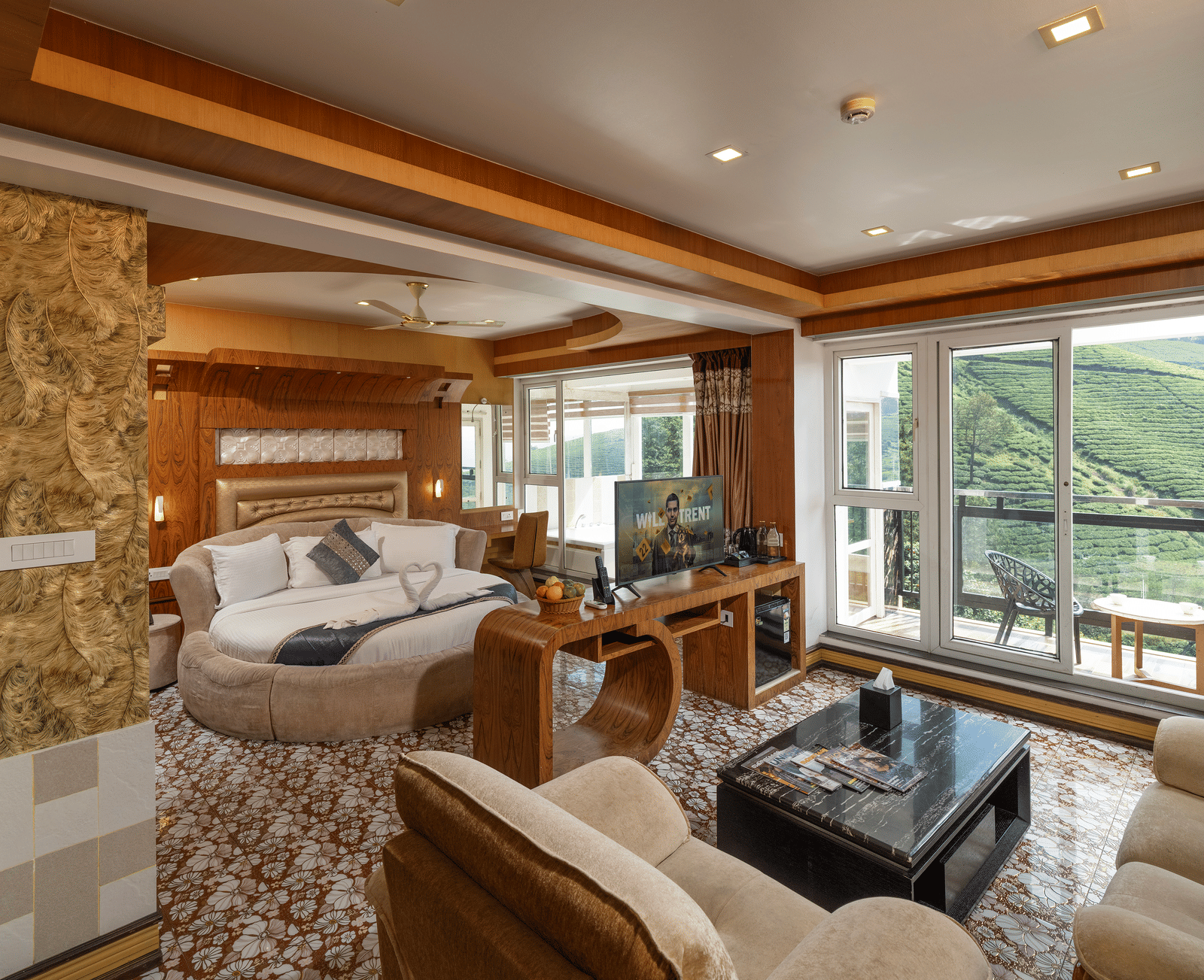 A living area of the Honey Moon Suite at Parakkat Nature Hotel and Resorts, Munnar, featuring plush seating, wood-panelled accents, an opening towards bedroom, and large windows offering a view of the landscape.