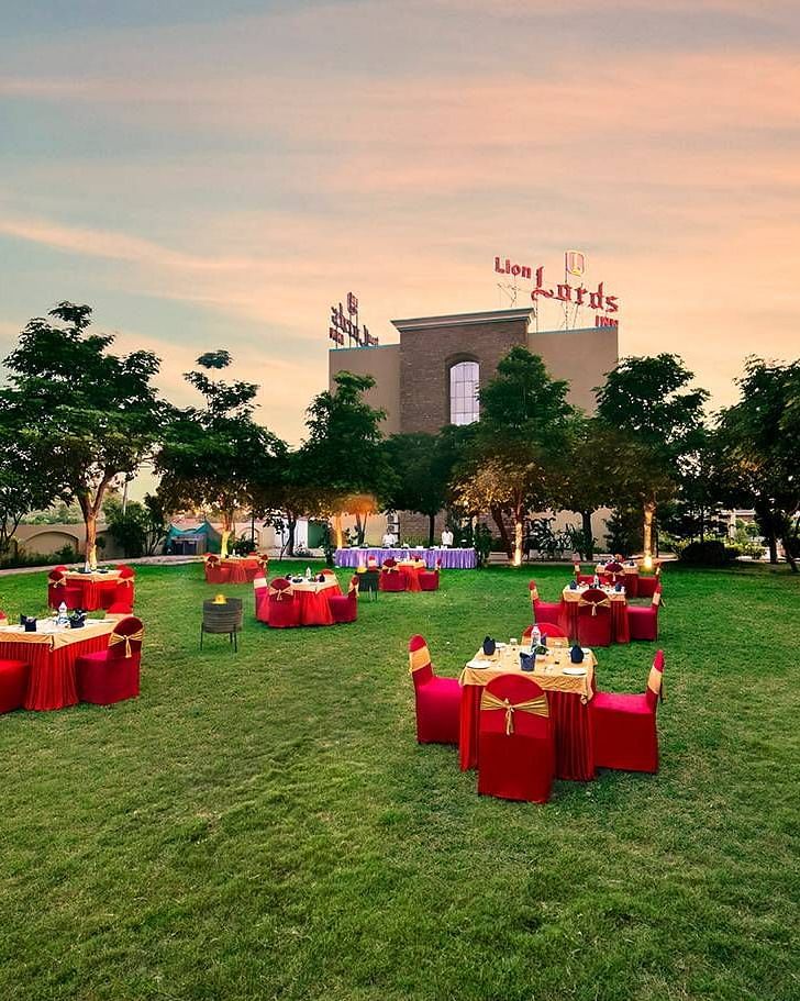 An outdoor area is prepared for an event with tables covered in red cloths on the grass - Lion Lords Inn Rajula