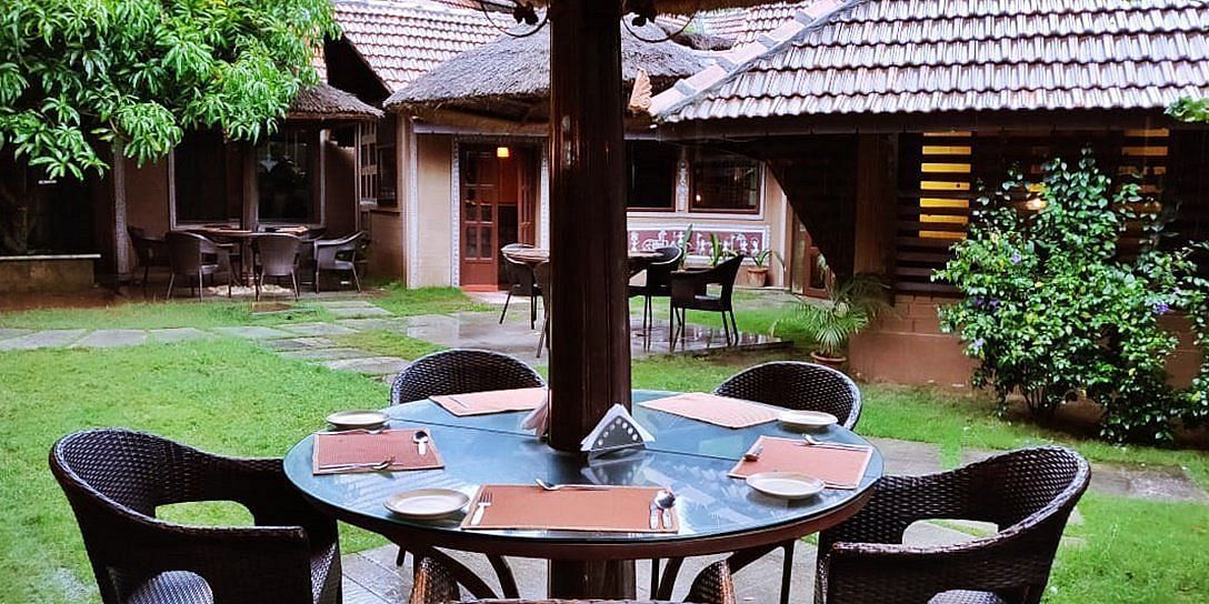 image of an outdoor dining area at hoysala village resort with four chairs surrounding a round glass top table.