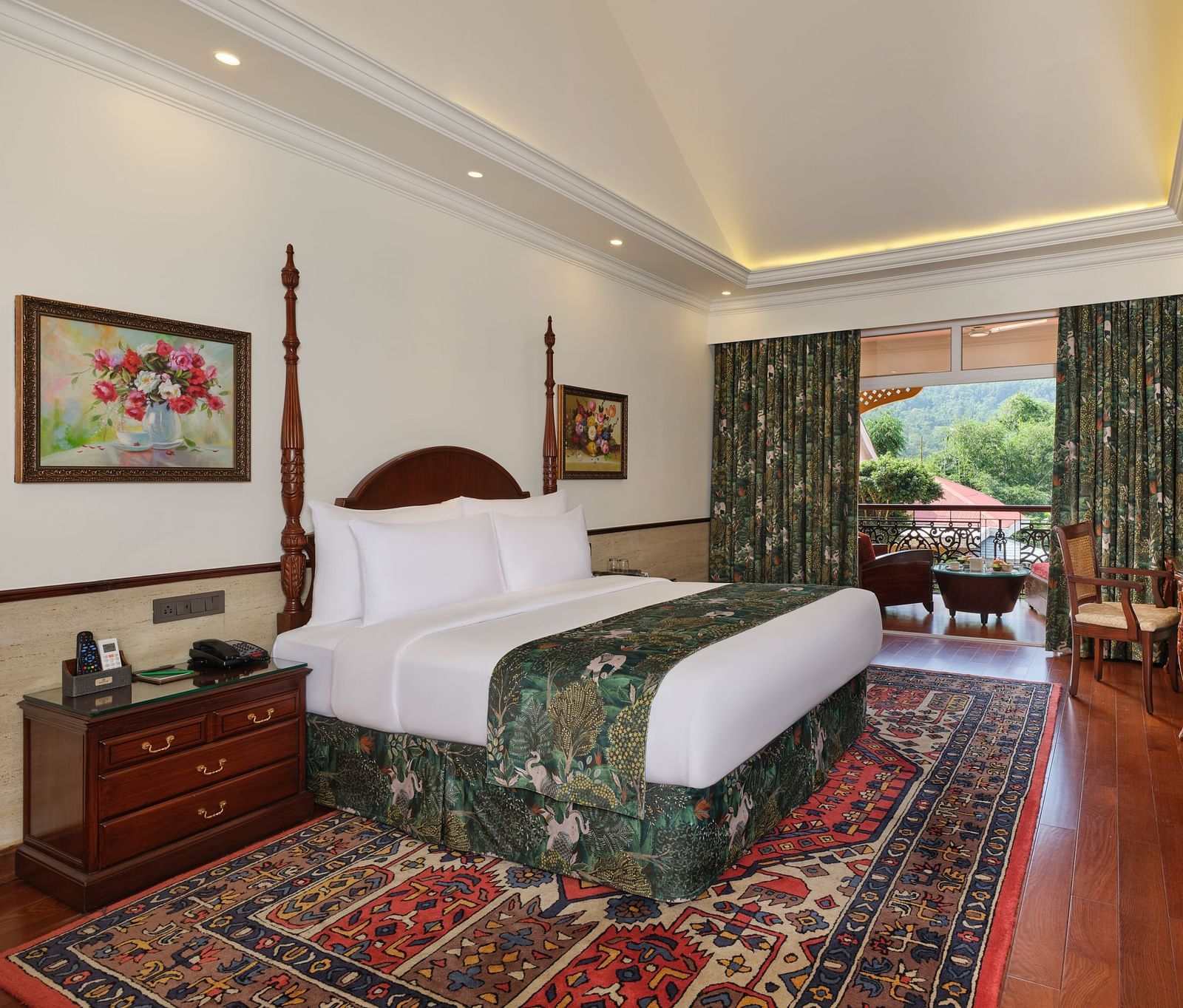 a Deluxe bedroom with a large bed on a decorative rug, wooden cabinet, TV, artworks, and a window overlooking greenery 