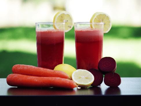 2 glasses of red juice with lemon slices, alongside fresh carrots, whole lemons, and sliced beets on a table at YO1 Longevity & Health Resorts
