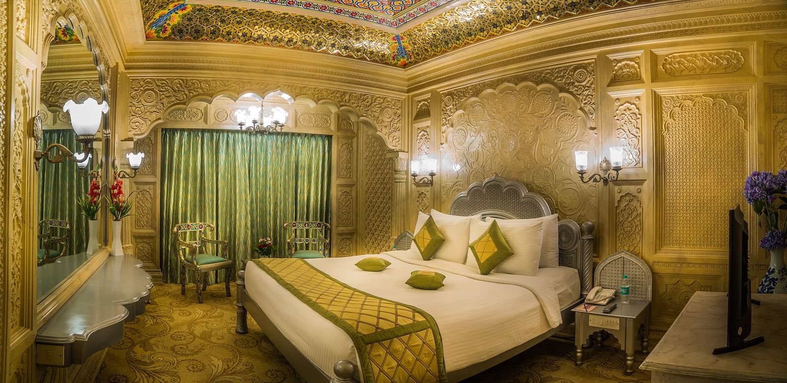A sumptuous hotel room that combines luxury with cultural artistry, featuring elaborate woodwork and plush furnishings A grand hotel suite with an opulent red and white decor, large bed, and seating area, reflecting a traditional style at Sitara Luxury Hot