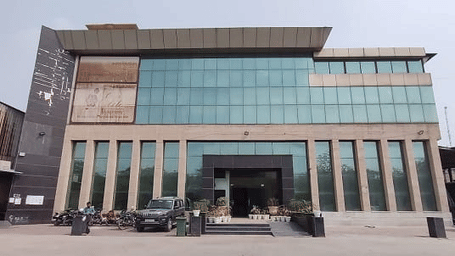 Exterior view of a multi storey commercial building featuring modern architectural design, main entrance, parked vehicles in front of the structure.