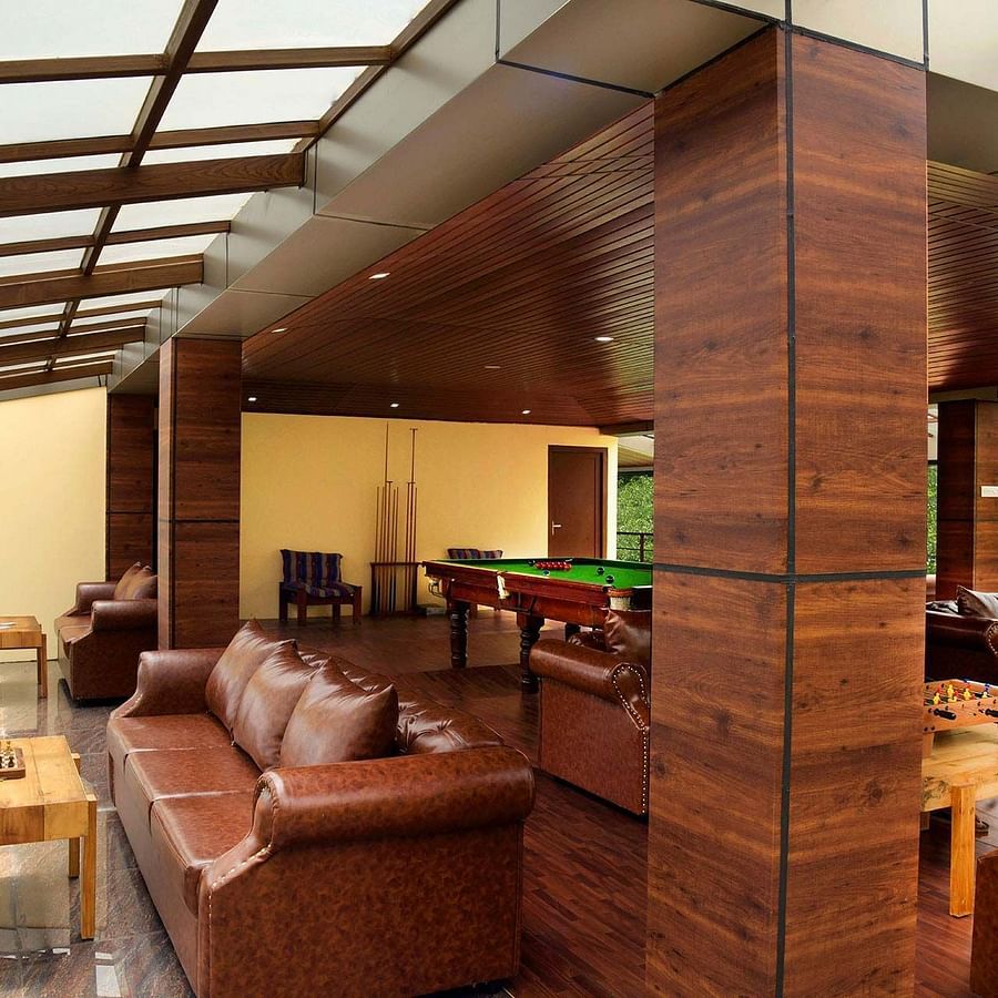 Shot of the indoor play area at the villa with brown sofas around Shot of the balcony at the villa with chairs kept | Ibex Stays and Trails, Valparai (Tale Rock)