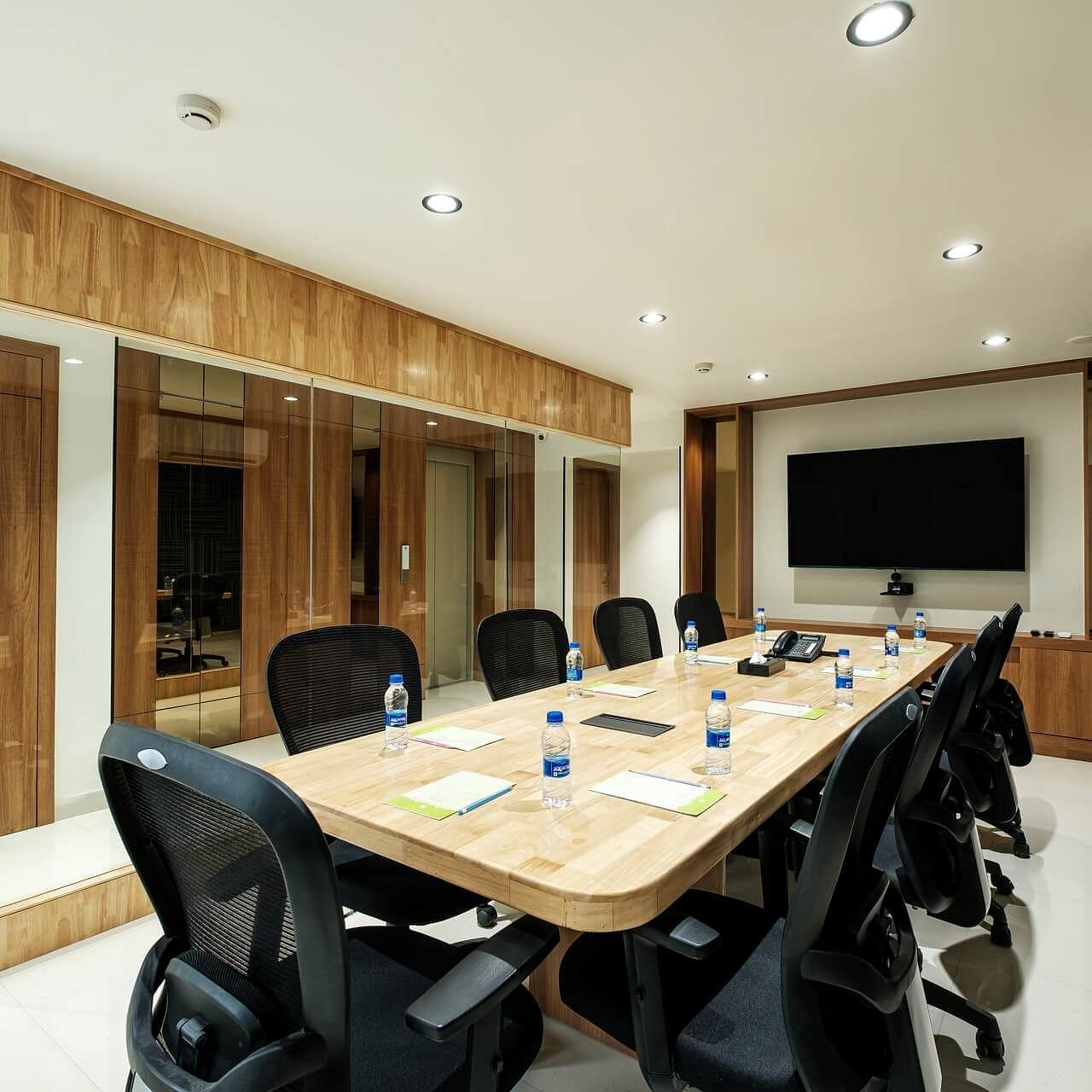 Diagonal view of the full boardroom at Indie Stays, Jaipur, with chairs along the sides, a screen at the front, and a wall-mounted AC.
