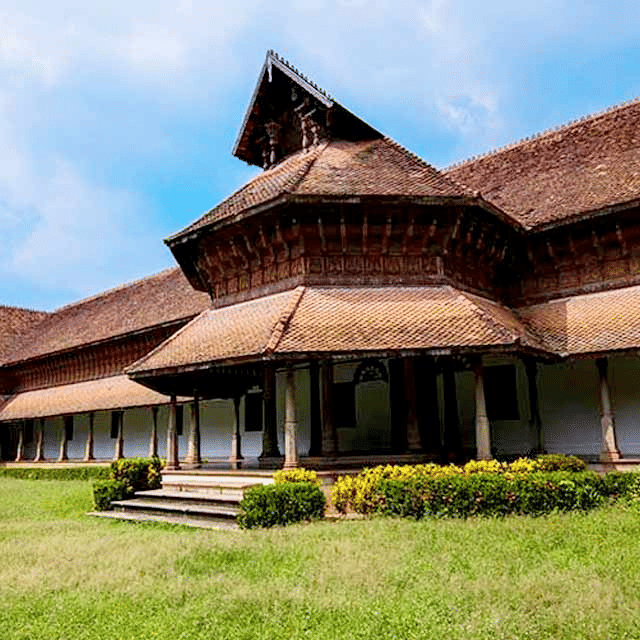 A traditional wooden-roofed structure with multiple sloping roofs set amid green trees.