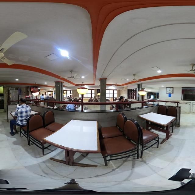 Dining area at Hotel Swagath, Bangalore with neatly arranged tables, cushioned chairs, and arched red ceiling design.