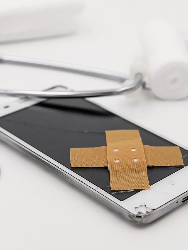 A broken smartphone with a plaster on its screen lies amongst medical supplies like a stethoscope.