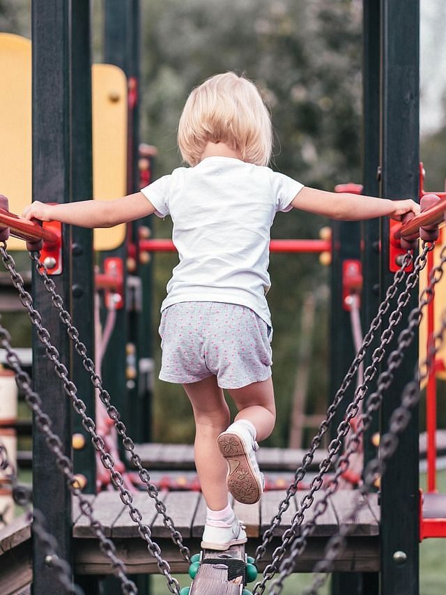 A small child confidently navigating a rope bridge on a playground.