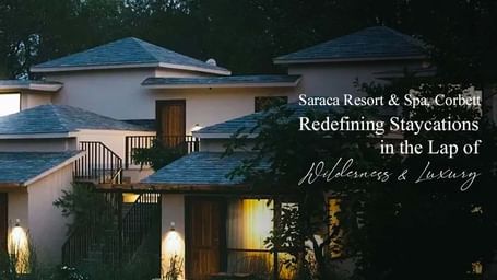 Night view of Saraca Resort & Spa, Corbett, with warmly lit villas surrounded by greenery, text overlay: Saraca Resort & Spa, Corbett: Redefining Staycations in the Lap of Wilderness & Luxury.