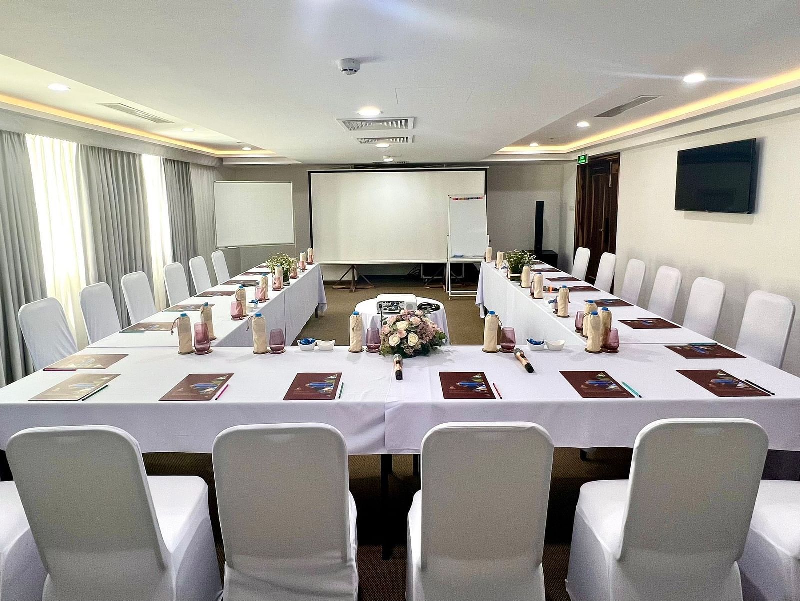 A front view of our meeting room with u-shaped table facing a projector and ambient lighting - Alibu Resort
