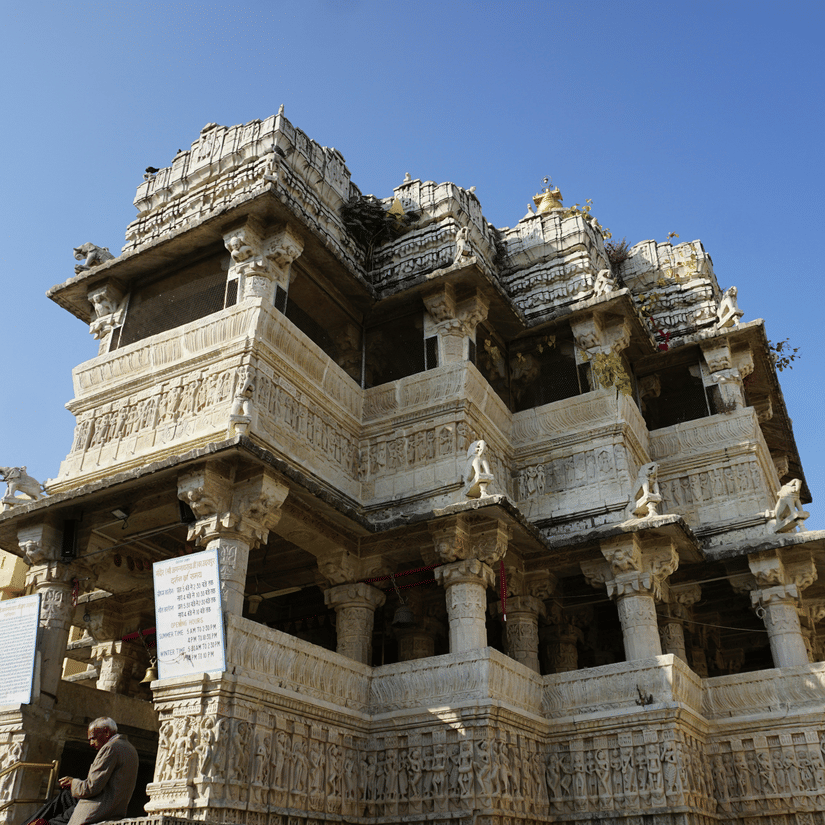 Multi-storey Jagdish temple with detailed carvings, pillars, and sculpted balconies against a clear blue sky