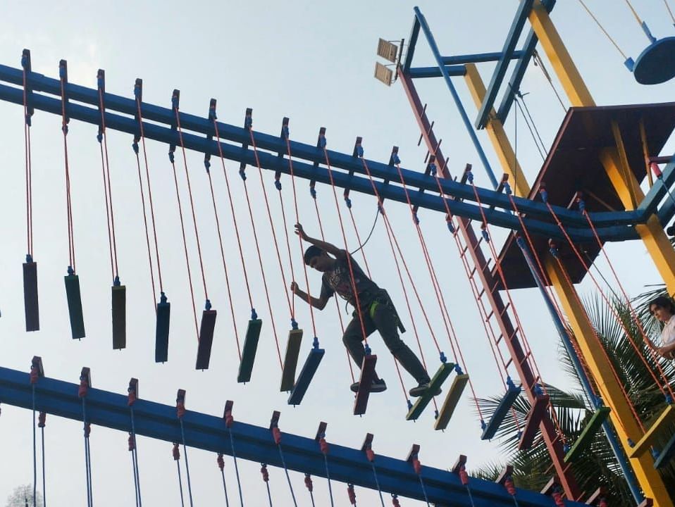 Silhouetted figures climb an outdoor adventure course structure with ropes and ladders