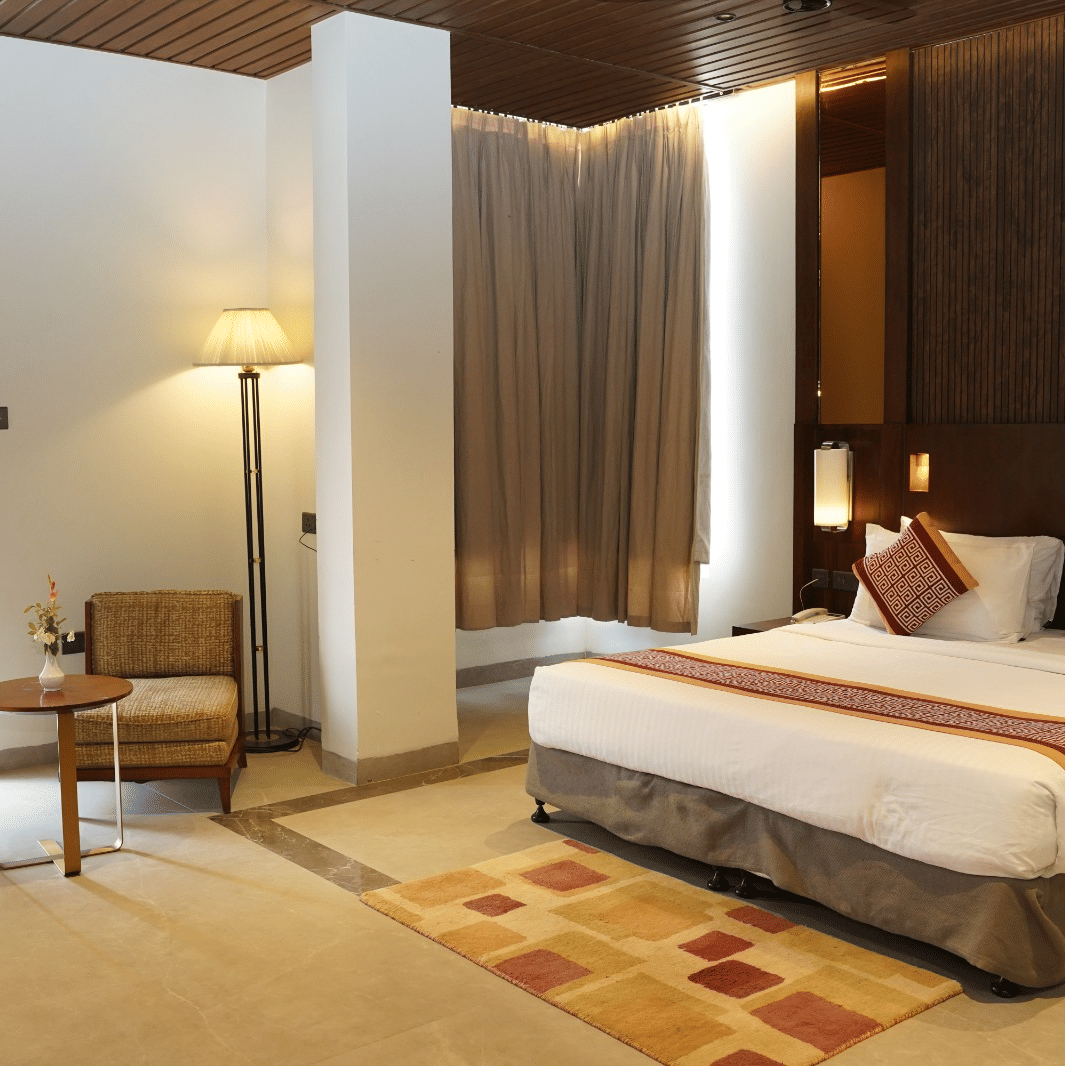 A bedroom including a king size bed, bedside lamps, 2 armchairs, and a floor lamp at Ananta Express, Jaunpur.