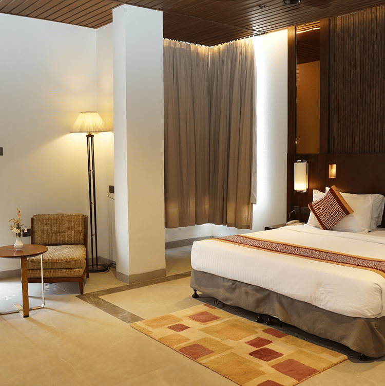A bedroom including a king size bed, bedside lamps, 2 armchairs, and a floor lamp at Ananta Express, Jaunpur.