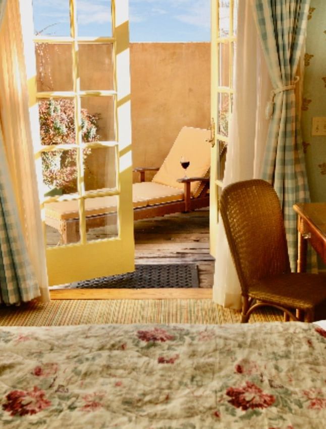 Lower Garden Room at Tallman Hotel featuring cozy bedding, a bedside table with a lamp on it, a balcony door opening to a private seating area in the balcony.