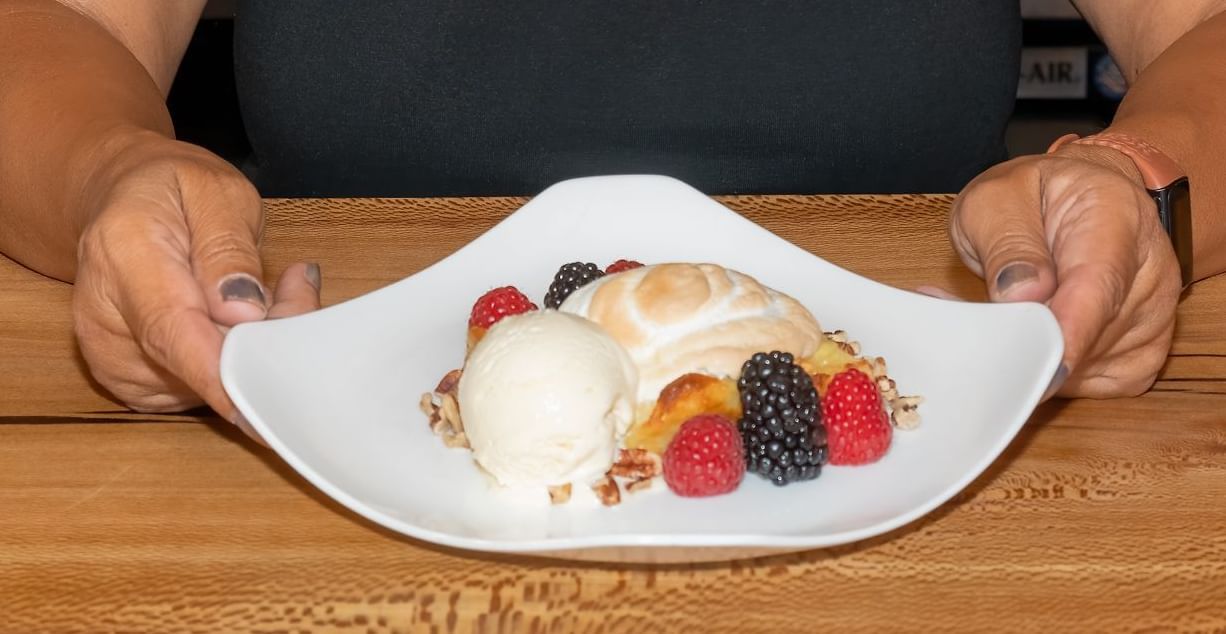 Smiling woman seated at the bar with a plated dessert in front of her at The Groveland Hotel.