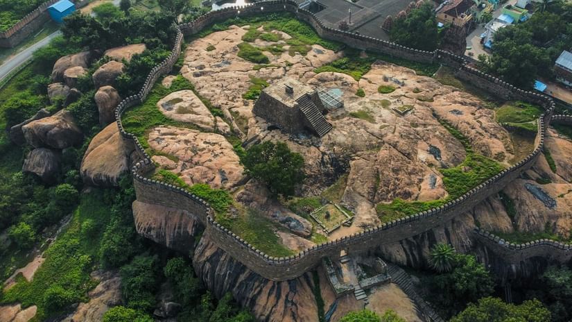 A stone fort on top of a hill, with outer ring walls and surrounded by trees.