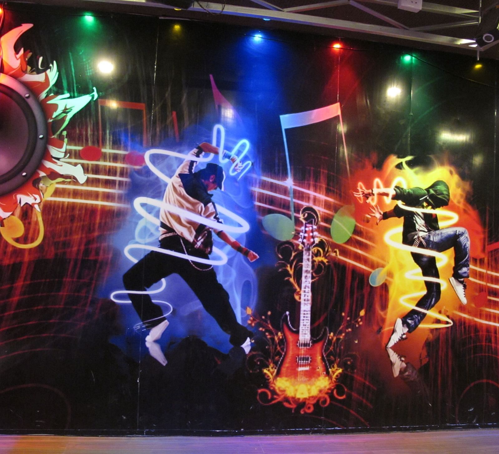 A close-up view of the wall mural, showcasing energetic dancers and dynamic light effects - TGI Apple Inn, Jaipur 